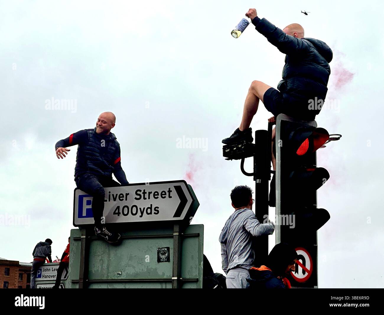 Fußballfans klettern am 26. Mai 2025 auf Ampeln und Schildern auf der Strand Street, Liverpool, Großbritannien, um die Siegerparade der Premier League zu sehen. - Smartphone-aufgenommenes Stockfoto