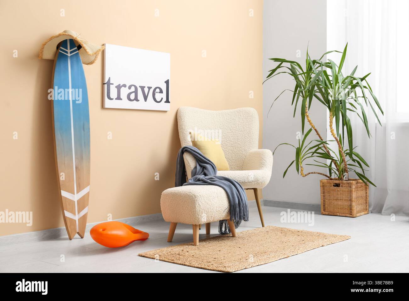 Inneneinrichtung des stilvollen Wohnzimmers mit weißem Sessel, Schwimmbrett, REISEPOSTER und Surfbrett Stockfoto