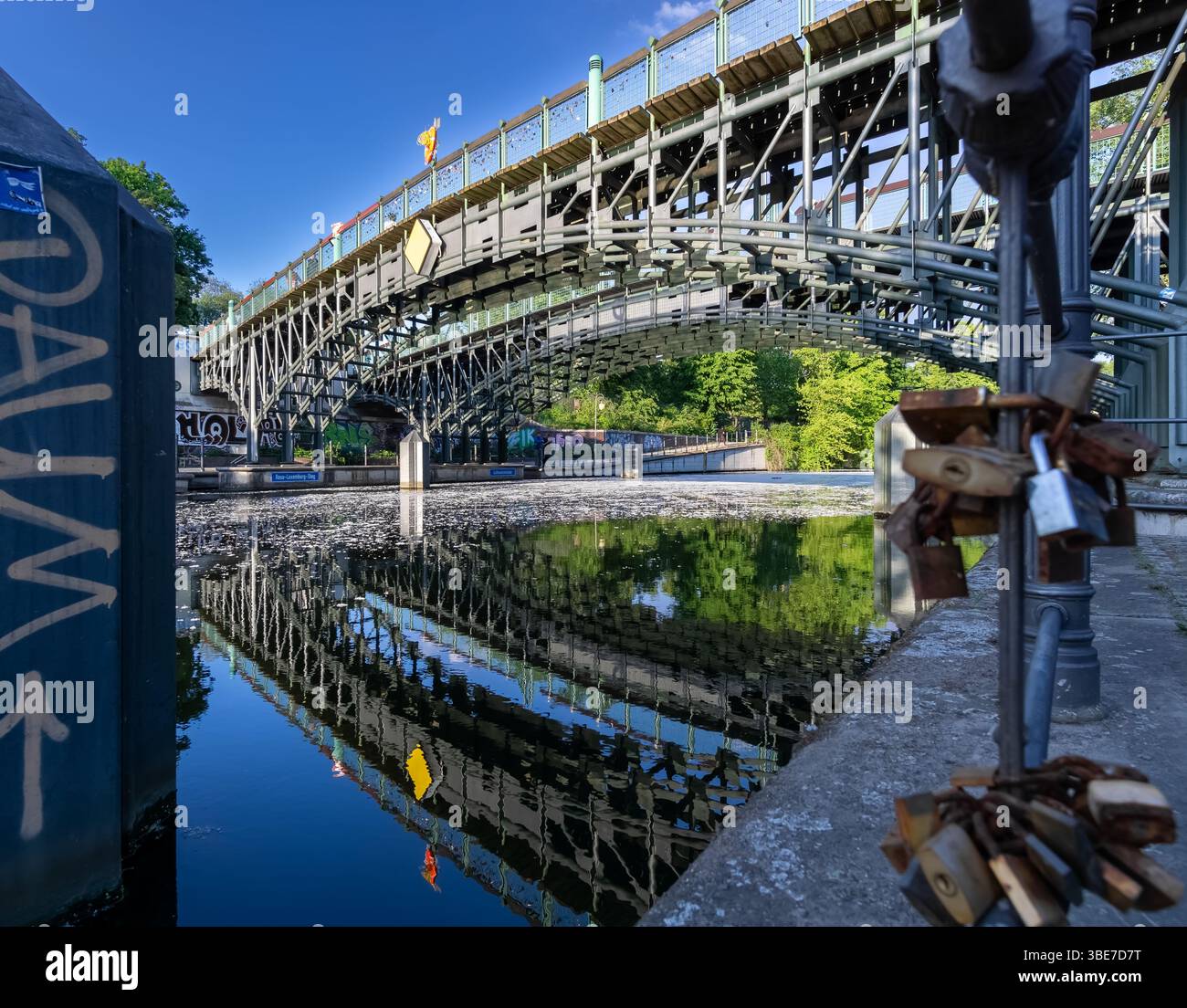 Lichtensteinbrücke über Berlins Landwehrkanal mit Metallschlössern im Vordergrund und Reflexionen auf dem ruhigen Wasser an einem sonnigen Frühlingstag. Stockfoto
