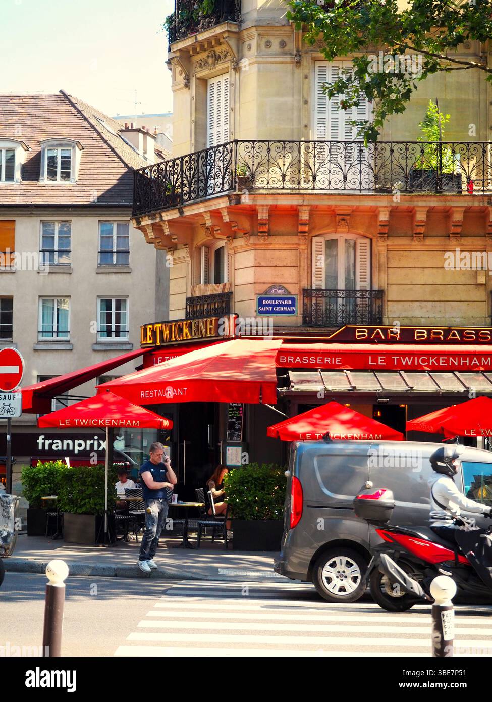 Brasserie Le Twickenham mit roten Sonnenschirmen an einer sonnigen Pariser Straßenecke, die Architektur und das Straßenleben im Haussmann-Stil zeigt Stockfoto