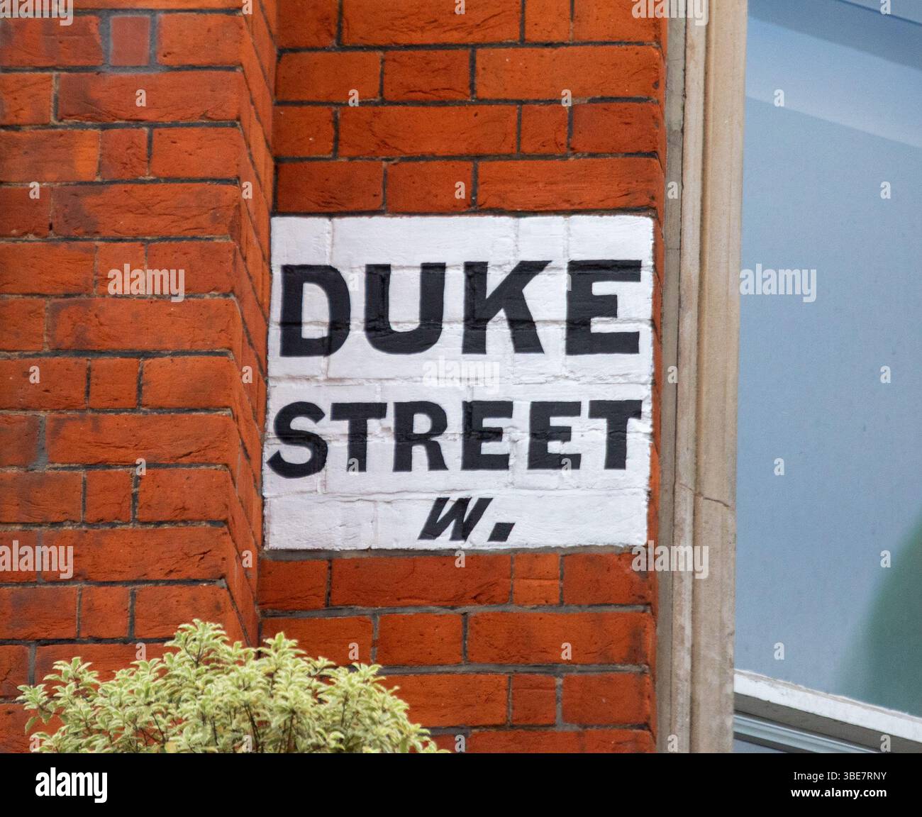 Straßenschild für Duke Street an einer roten Backsteinmauer in London. Das Schild ist in kräftiger schwarzer Schrift auf weißem Hintergrund gehalten. Stockfoto