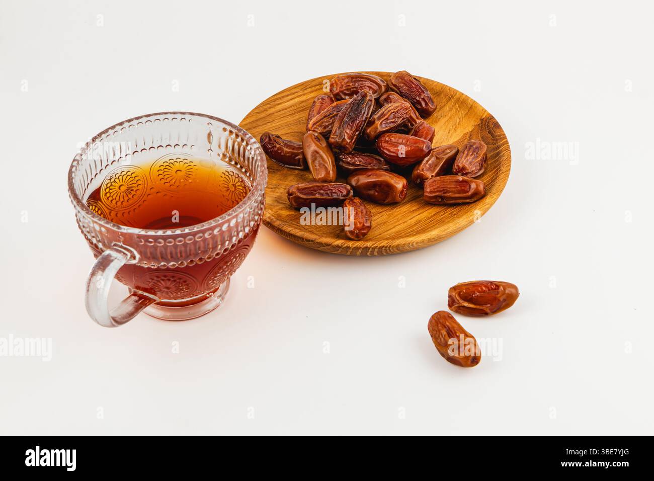 Ein Glas aromatischen Tee steht neben einem Holzteller mit süßen, prallen Datteln und sorgt für ein köstliches Snack-Arrangement für jeden Anlass. Stockfoto
