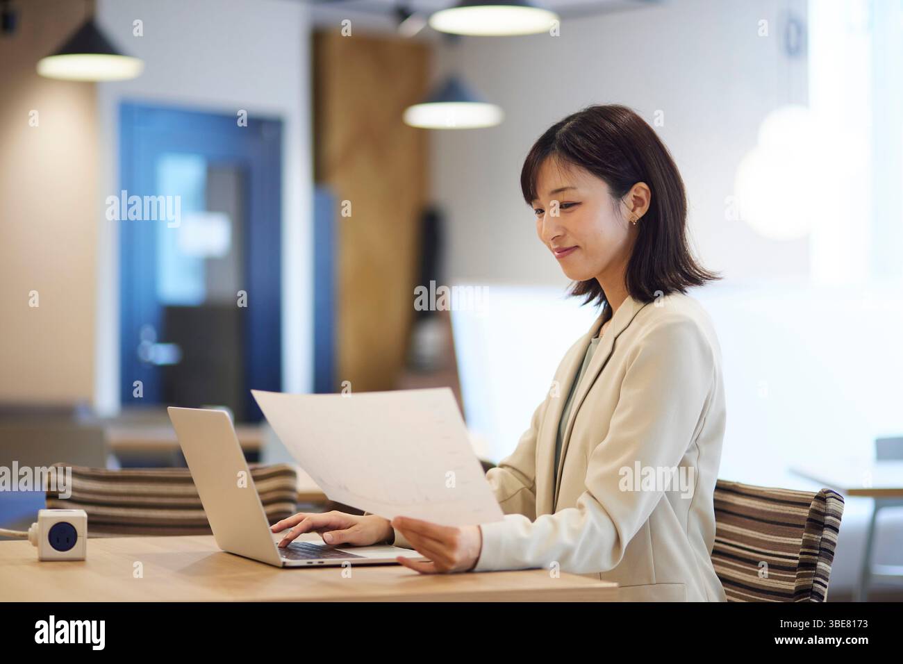 Lächelnde japanische Geschäftsfrau, die im Büro an ihrem Laptop arbeitet Stockfoto