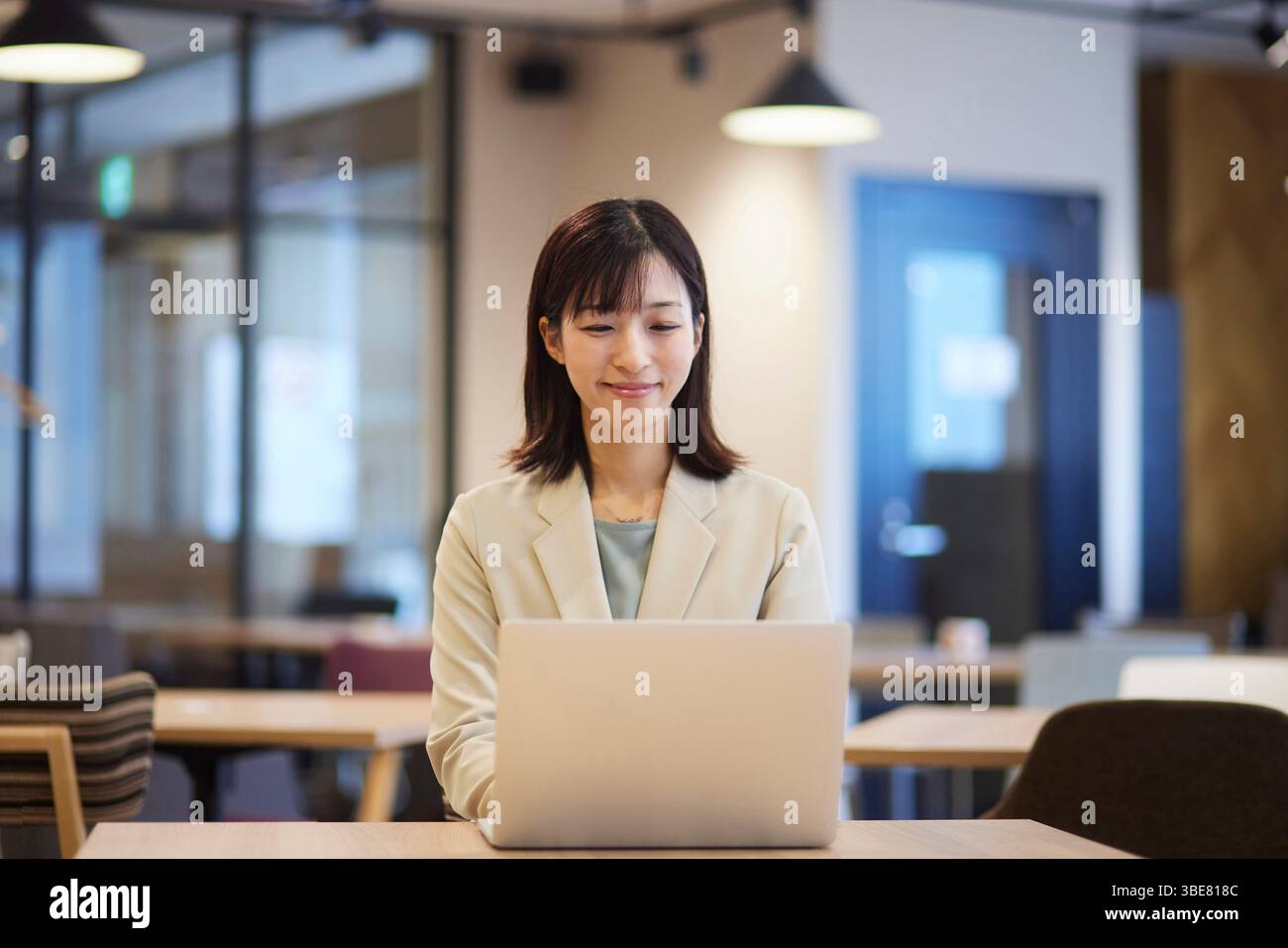 Lächelnde japanische Geschäftsfrau, die im Büro an ihrem Laptop arbeitet Stockfoto