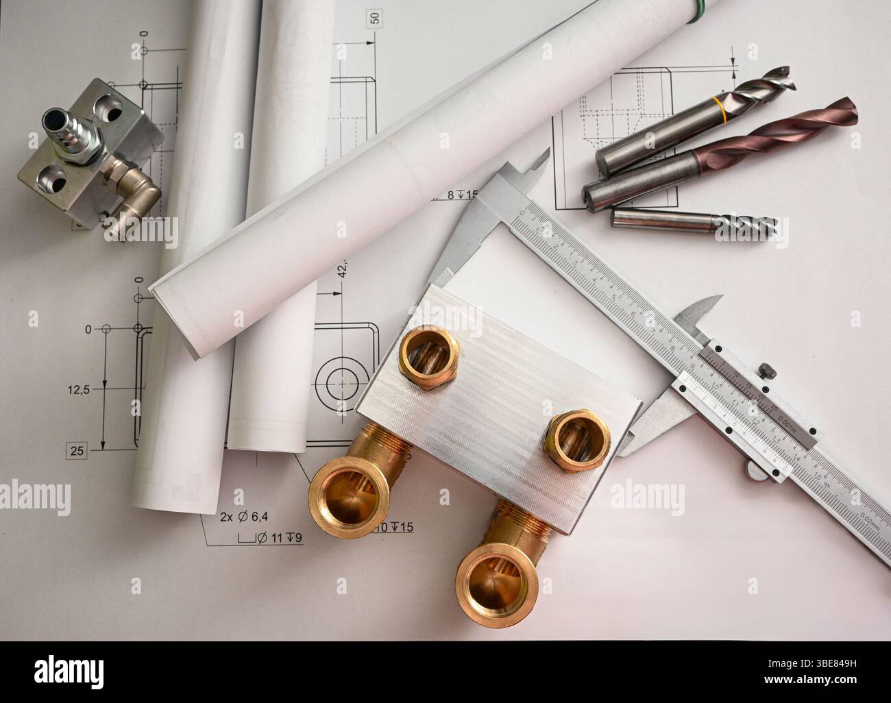 Installationen, Bremssattel, Bohrer und gewalzte Baupläne auf dem Tisch symbolisieren den Konstruktions- und Fertigungsprozess. Stockfoto
