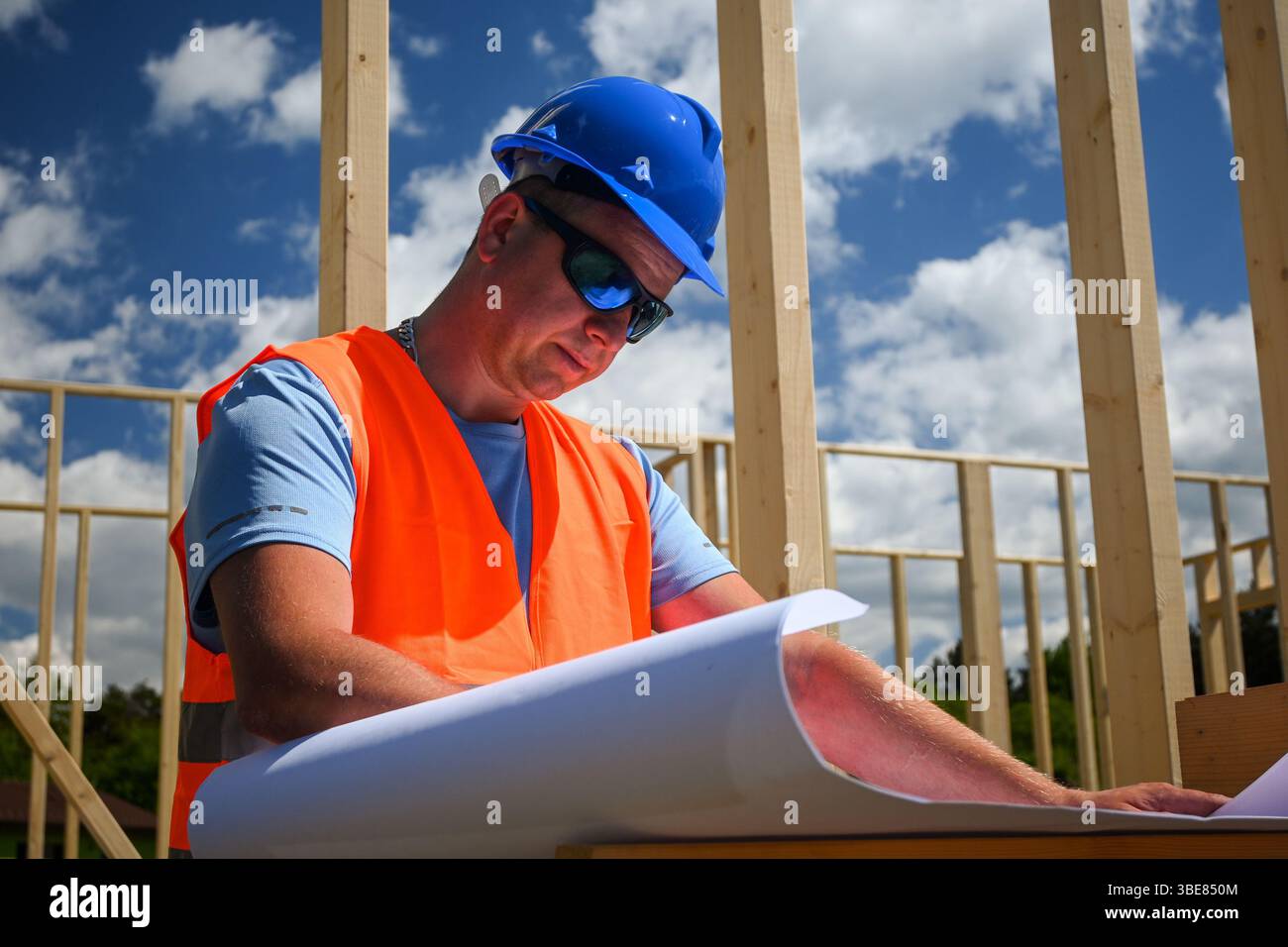 Bauarbeiter untersucht Baupläne auf einer Baustelle unter hellblauem Himmel. Stockfoto