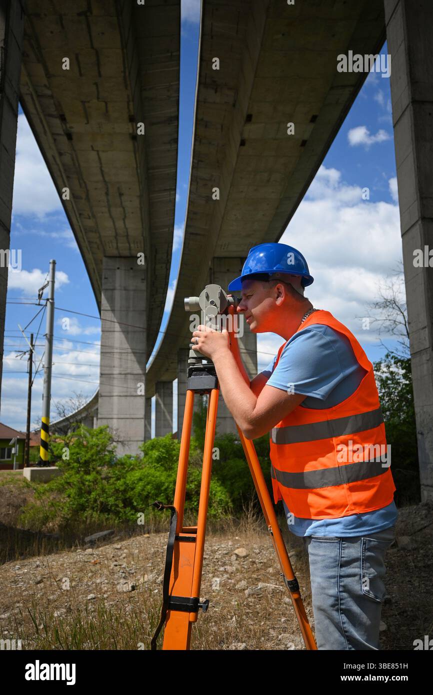 Vermesser, der Messungen mit Theodolit unter einer Autobahnüberführung durchführt, um genaue Daten für Bau- oder Instandhaltungsprojekte zu gewährleisten. Stockfoto