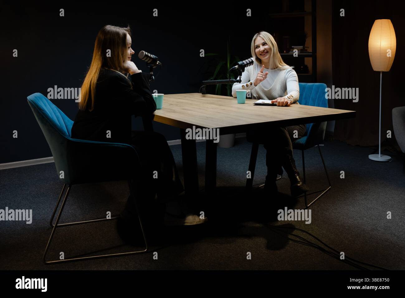 Zwei glückliche Podcasterinnen nehmen eine neue Episode auf, sprechen und lachen in einem professionellen Aufnahmestudio Stockfoto