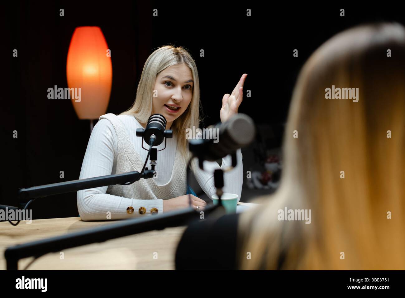 Zwei glückliche Podcasterinnen nehmen eine neue Episode auf, sprechen und lachen in einem professionellen Aufnahmestudio Stockfoto