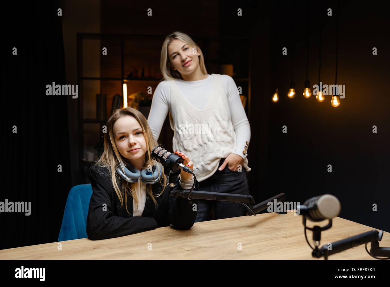 Zwei weibliche Podcasterinnen, die während der Live-Aufnahme in einem professionellen Studio eine gute Geste machen und Selbstvertrauen und Positivität ausstrahlen Stockfoto