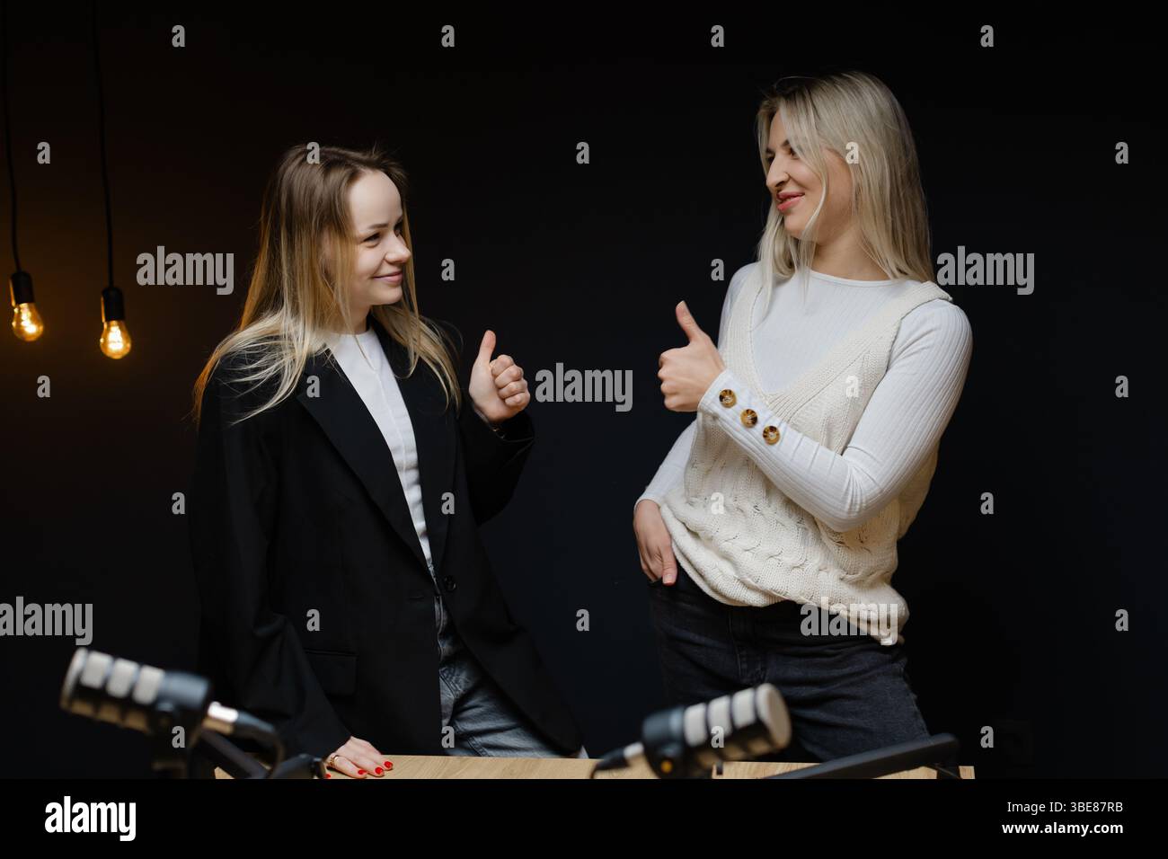 Zwei weibliche Podcasterinnen zeigen und lachen während einer Aufnahmesitzung in einem professionellen Studio und schaffen ansprechende Audioinhalte Stockfoto