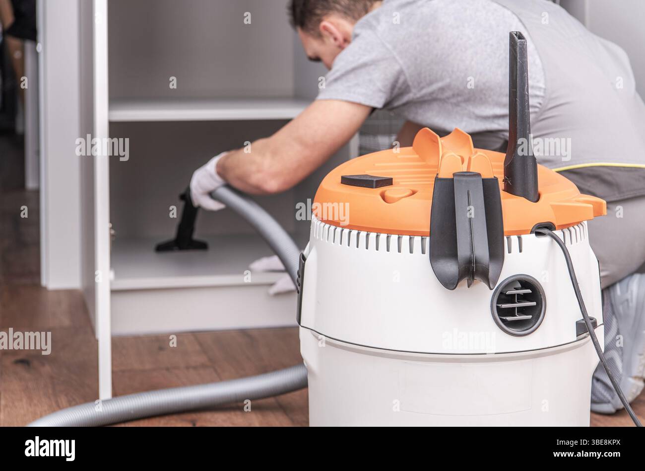 Eine Person saugt in einem Schrank in einer modernen Küche und konzentriert sich dabei auf das Entfernen von Staub und Schmutz. Die Küche ist hell durch natürliches Licht beleuchtet. Stockfoto