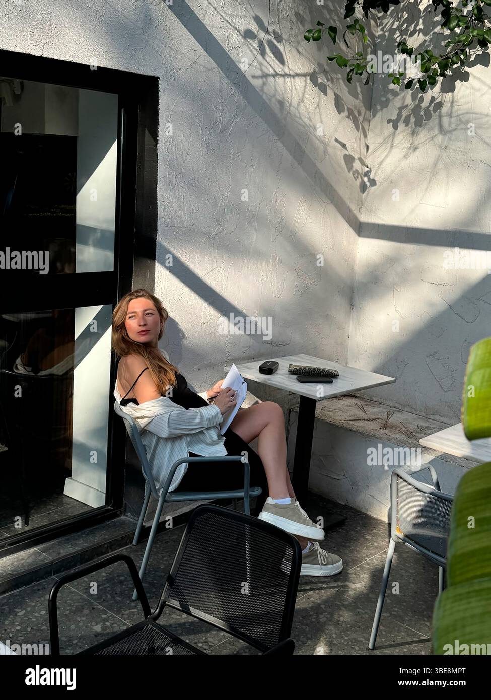 Eine junge Frau genießt einen sonnigen Nachmittag in einem gemütlichen Café im Freien in einer urbanen Umgebung Stockfoto