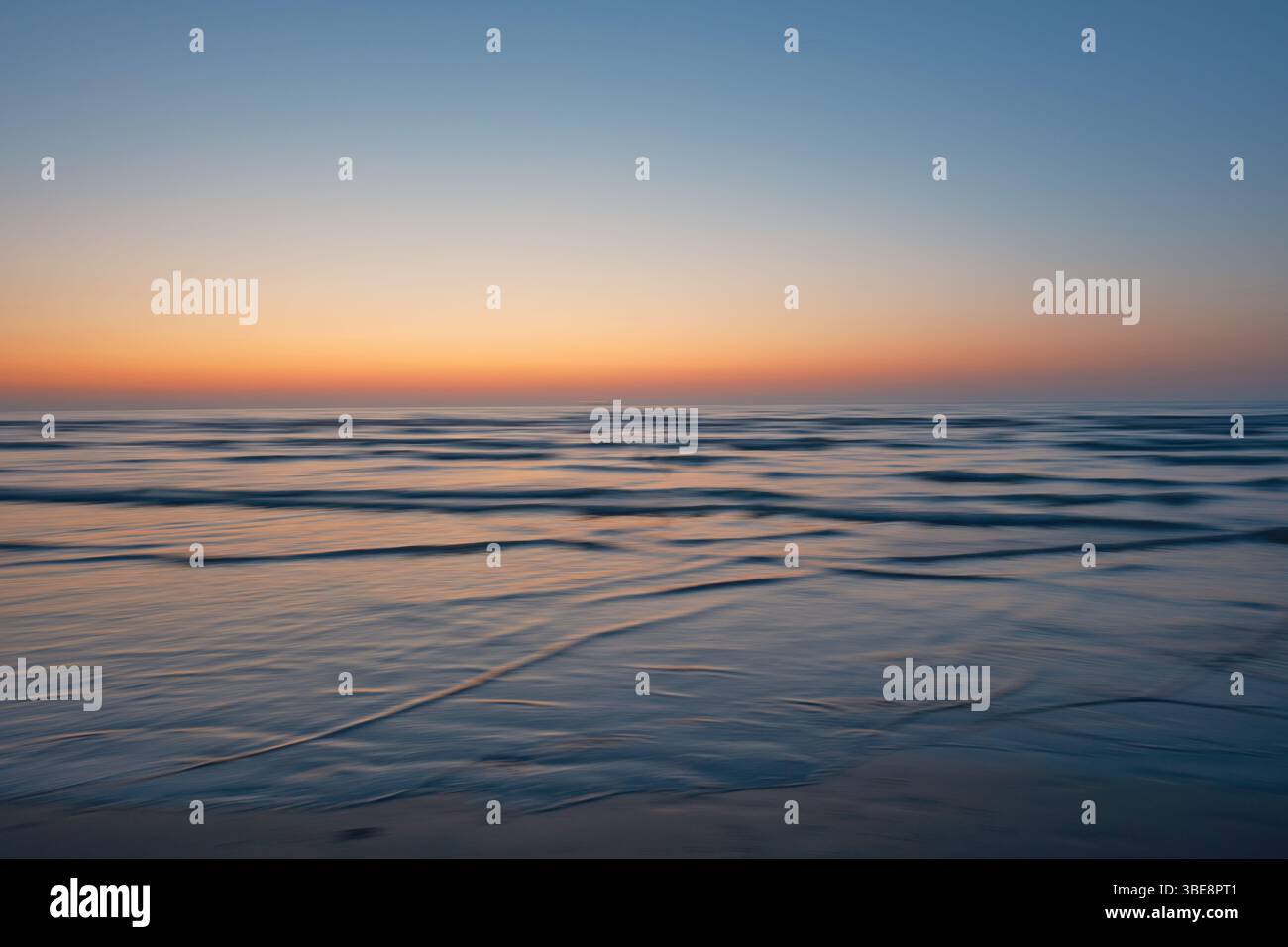 Friedlicher Sonnenuntergang über dem Meer in Dieppe, Normandie, mit ruhigen Wellen und sanften Pastelltönen, die sich nahtlos von Orange bis tiefem Blau vermischen. Stockfoto