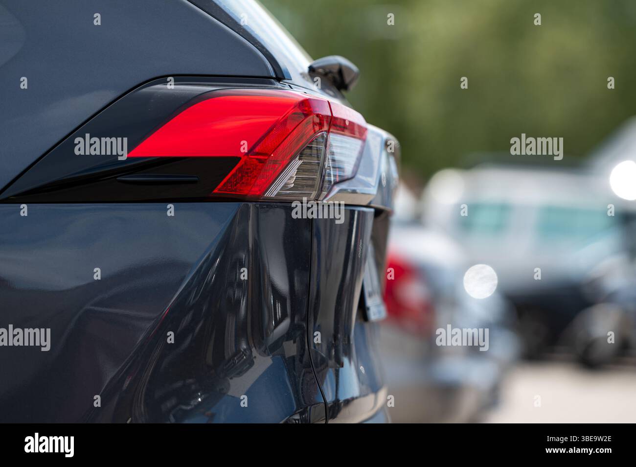 Ein leuchtend rotes Rücklicht eines geparkten Autos hebt sich an einem sonnigen Tag auf einem belebten Parkplatz ab. Stockfoto