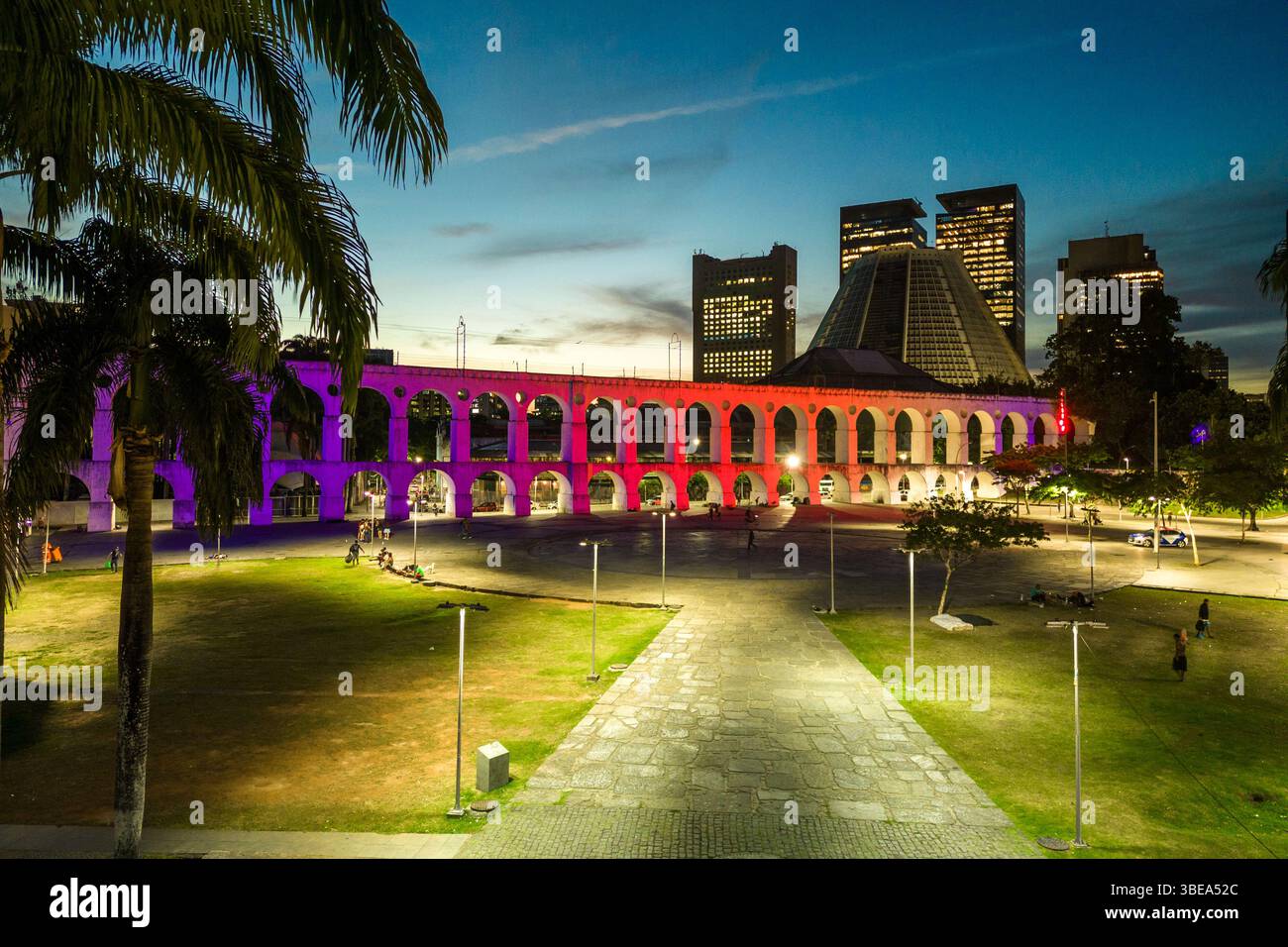 Lapa Aquädukt, beleuchtet mit violetten und rosa Farben am Abend mit hohen Bürogebäuden in der Innenstadt von Rio de Janeiro Stockfoto