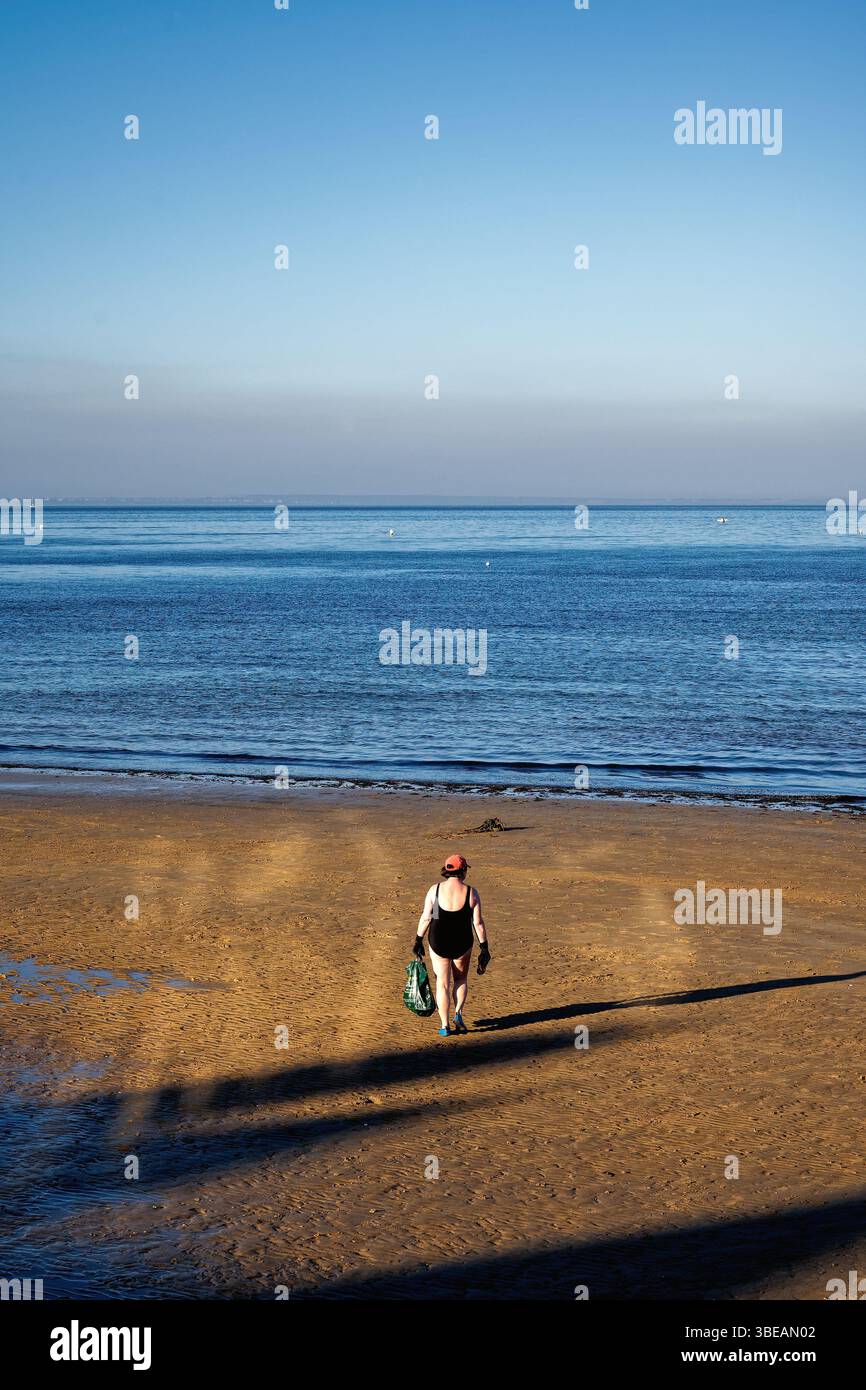 Rückansicht einer älteren Schwimmerin, die an einem Sommerabend in Swanage in Richtung Meer spaziert, Dorset England UK Stockfoto