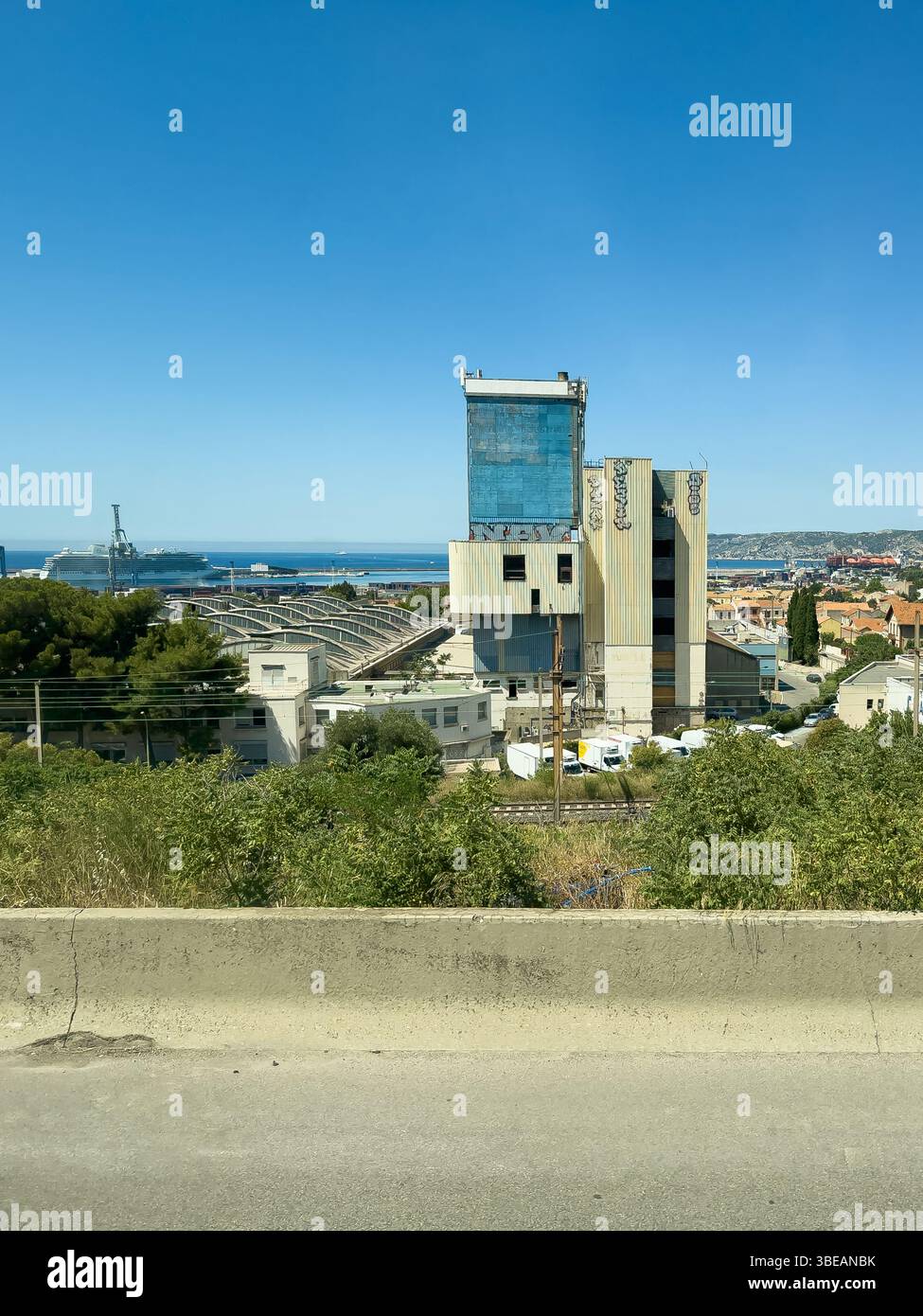 Marseille, Frankreich - 10. Juli 2024: Centralex Entrepots, Lagerhauskomplex mit Hafen dahinter und Kreuzfahrtschiff im Hafen von der Autobahn A55 aus gesehen Stockfoto