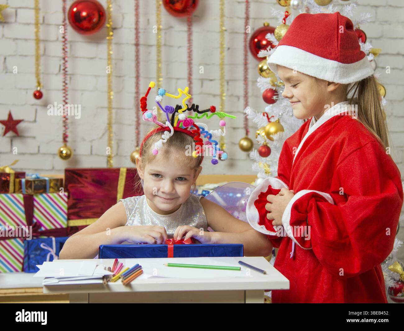 Mädchen sitzt an einem Tisch mit einem Bleistift und ein Blatt Papier mit einem Feuerwerk auf dem Kopf, Santa Claus ihr bereit, ihr ein Geschenk zu geben Stockfoto