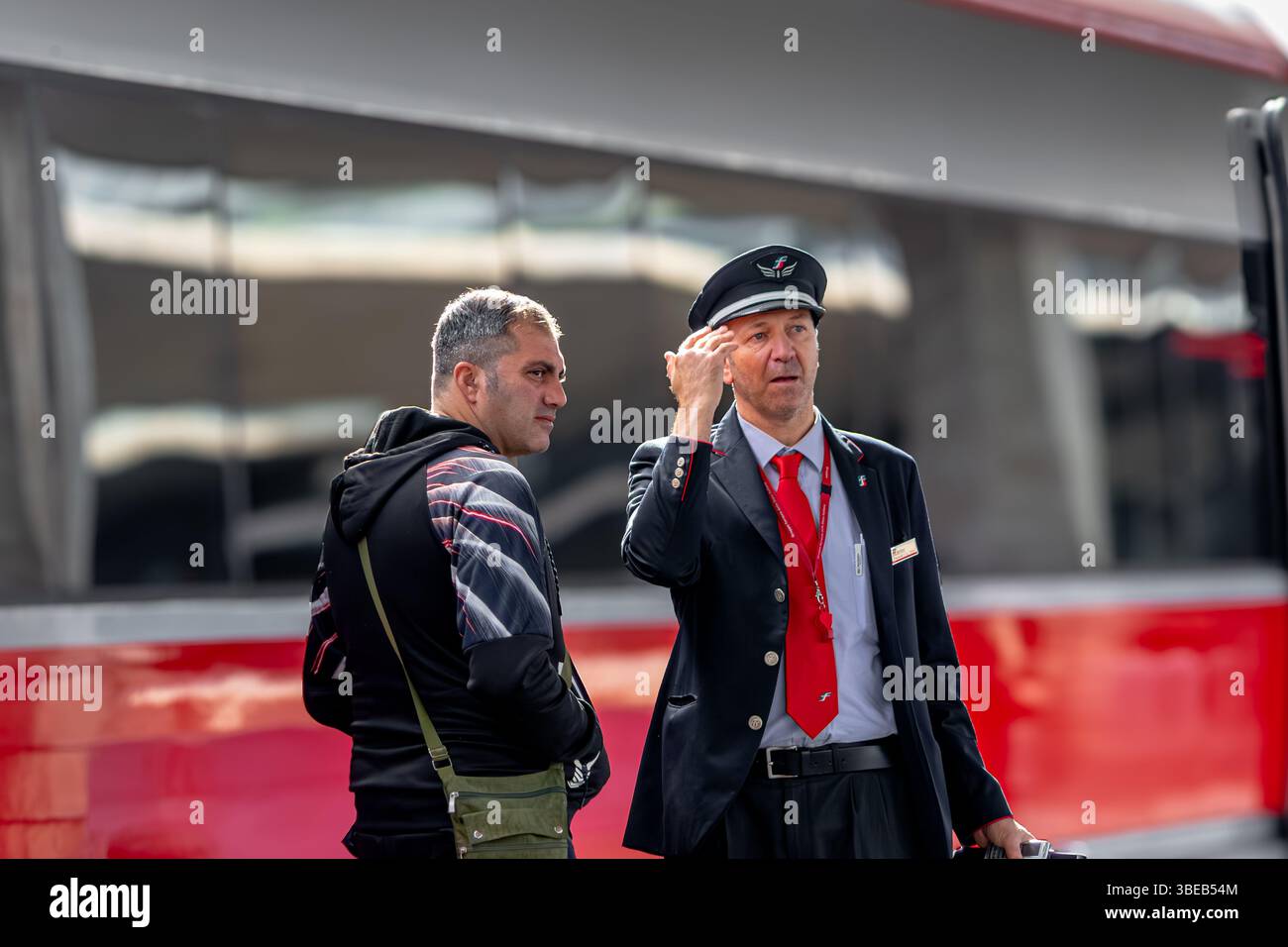 Ein italienischer Eisenbahnwächter aus Trenitalia, der einem Fahrgast auf dem Bahnsteig am Bahnhof Santa Maria Novella (SMN) in Florenz, Italien, hilft Stockfoto