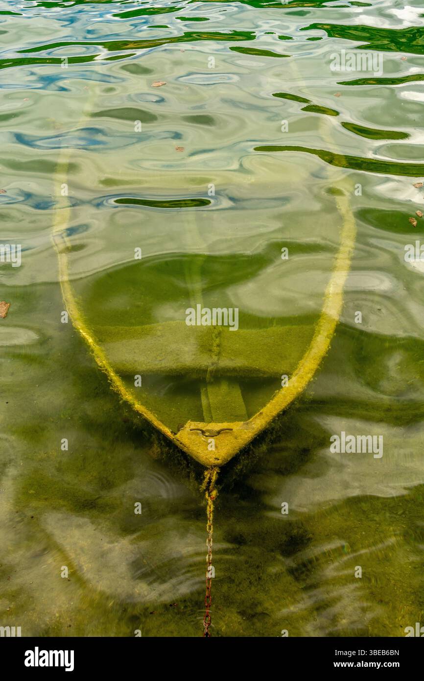 Ein kleines Boot, das teilweise in einem ruhigen See in Frankreich untergetaucht ist, zeigt seinen verwitterten Rumpf unter der Wasseroberfläche, umgeben von ruhigen Reflexen Stockfoto