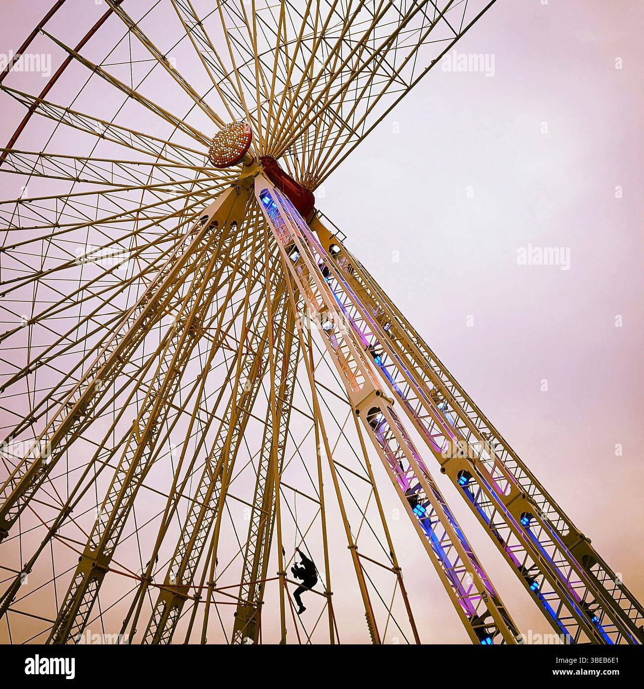 Ein Wartungspersonal kann die Struktur eines Riesenrads mit leuchtenden Lichtern besteigen. Stockfoto