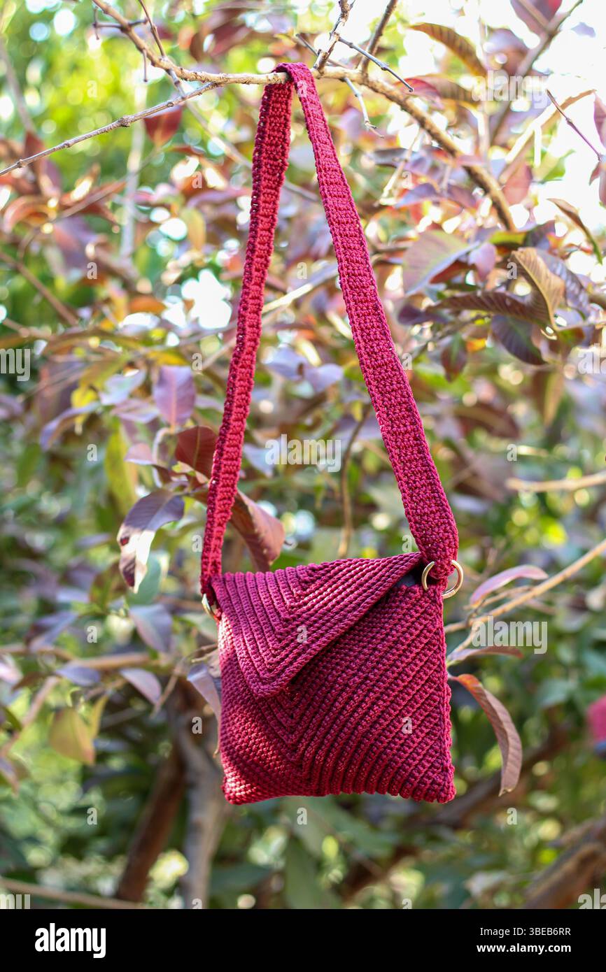 Rote Tasche häkeln, die an einem Zweig eines Baumes mit roten Blättern hängt. Handgefertigt. Stockfoto