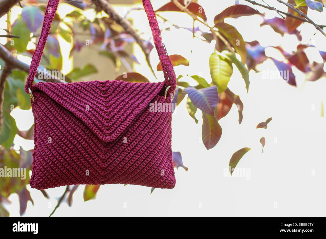 Rote Tasche häkeln, die an einem Zweig eines Baumes mit roten Blättern hängt. Handgefertigt. Stockfoto