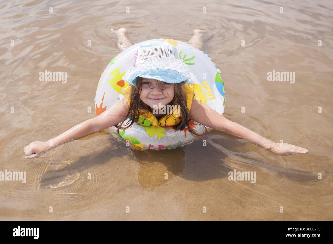 Kleines Mädchen im seichten Wasser liegend auf dem Bauch in den aufblasbaren Ring ausgestreckten Arme und Beine Stockfoto