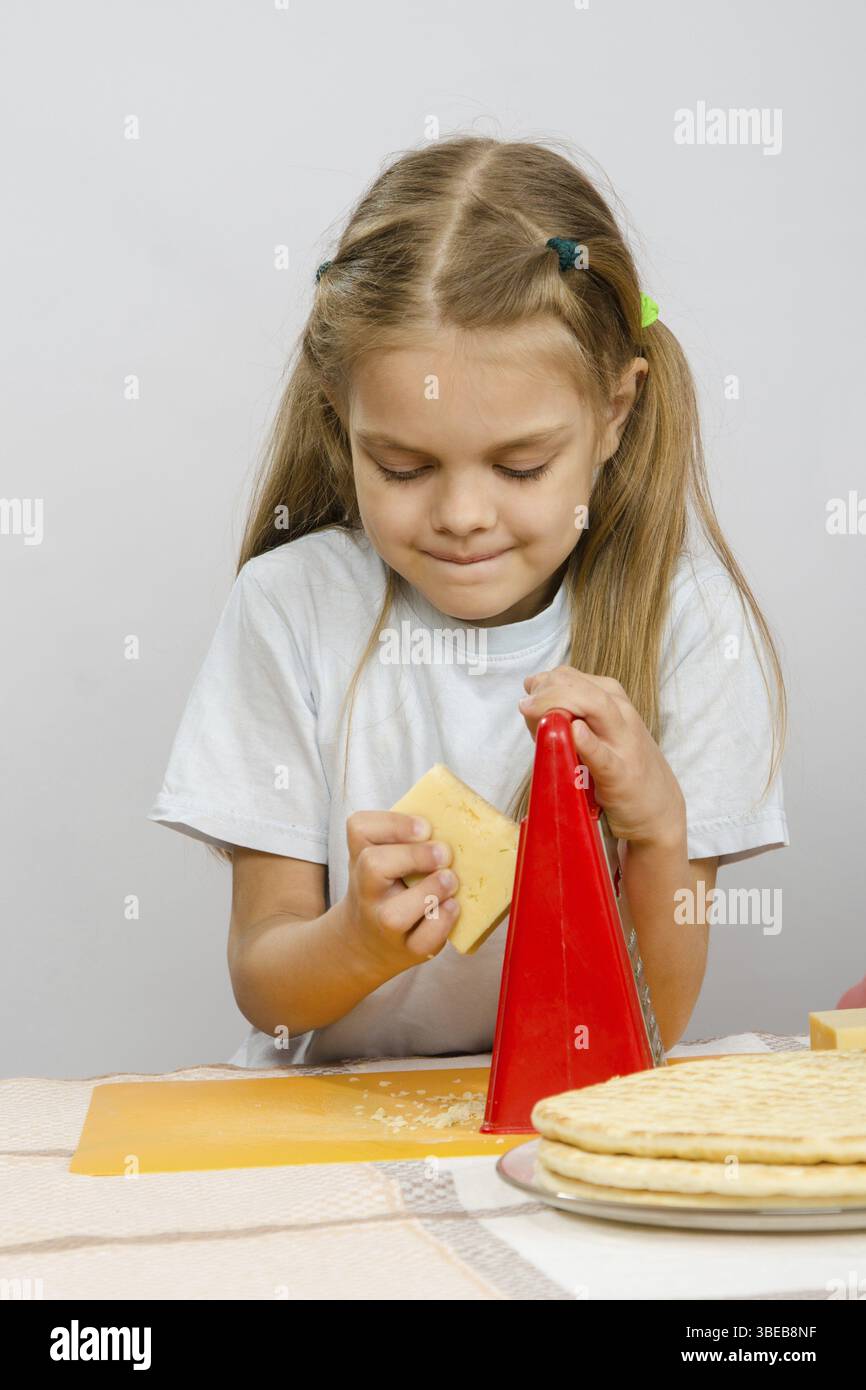 Sechsjährigen Mädchen posiert auf dem Küchentisch mit Käse und ein Reibeisen in den Händen der Stockfoto