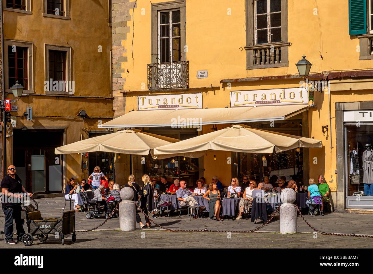 Leute sitzen draußen in der Sonne in Caffetteria Turandot auf der Piazza San Michele, Lucca, Italien Stockfoto