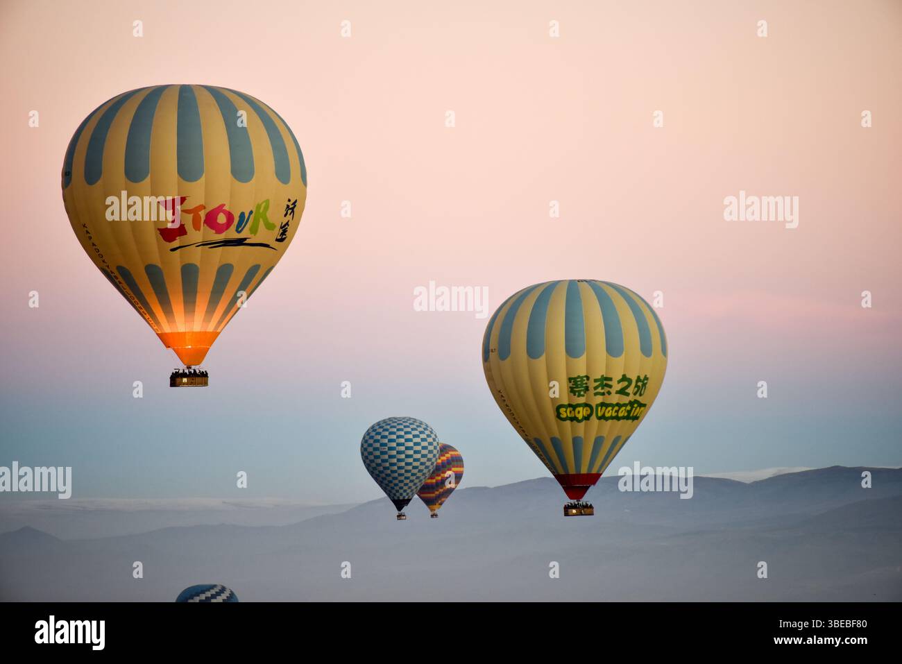 Farbenfrohe Heißluftballons steigen während des Sonnenaufgangs in den Himmel über Kappadokien und schaffen eine atemberaubende visuelle Darstellung vor weichem Morgenlicht. Stockfoto
