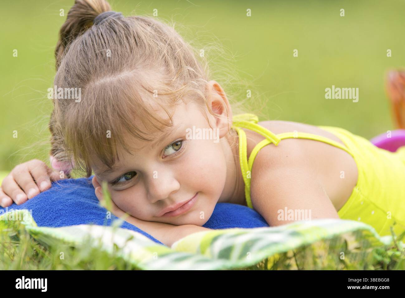 Fünfjähriges Mädchen liegt auf einem Bett auf einer grünen Wiese und schaut nachdenklich beiseite Stockfoto