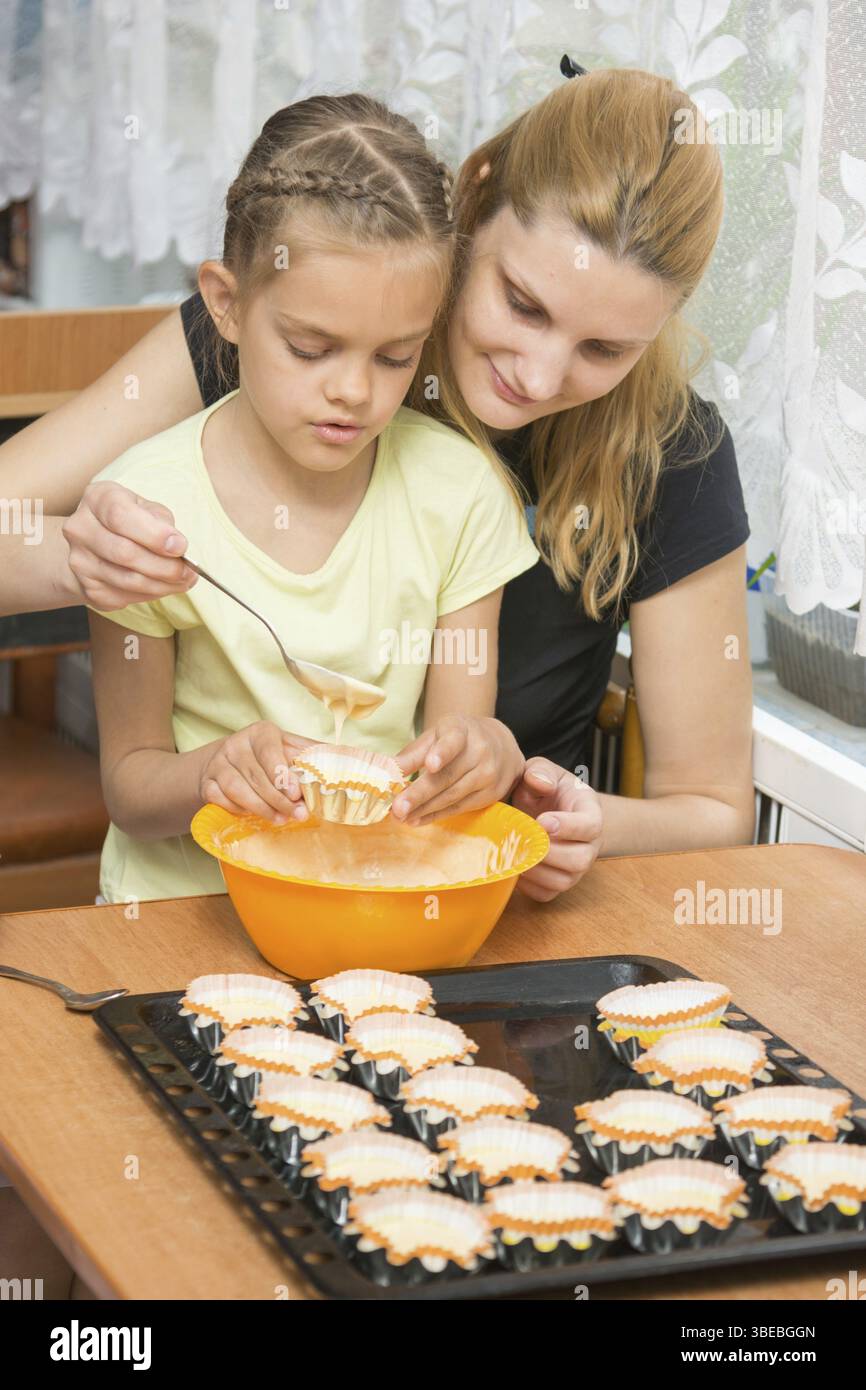 Mutter hilft Tochter pour Teig in die Form für cupcakes Stockfoto