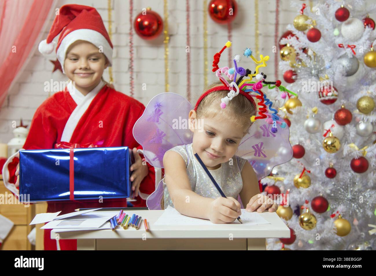Mädchen sitzt an einem Tisch mit einem Bleistift und ein Blatt Papier mit einem Feuerwerk auf dem Kopf, Santa Claus ihr bereit, ihr ein Geschenk zu geben Stockfoto