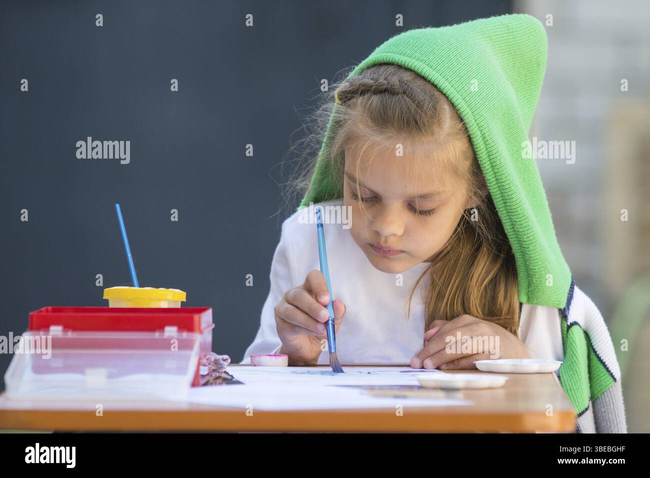 Etwas zerzaust Mädchen Aquarell malt sitzt am Tisch im Hof Stockfoto