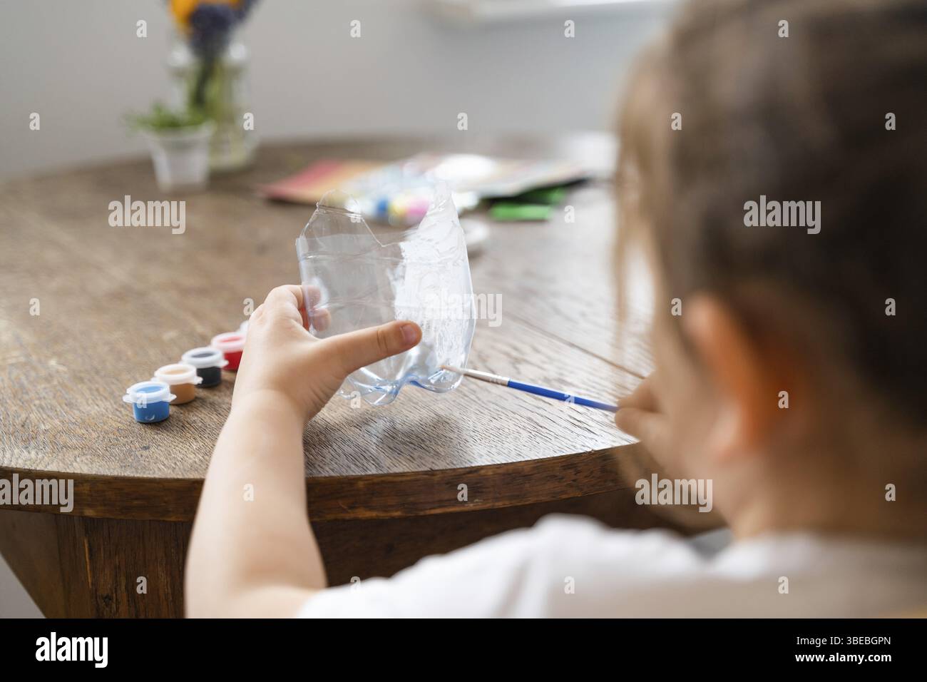 Kaukasisches Vorschulmädchen bastelt mit Plastikflasche und Farben. Recyceln Sie Upcycling-Abfälle. Nachhaltiger Lebensstil. Hochwertige 4K-Aufnahmen Stockfoto