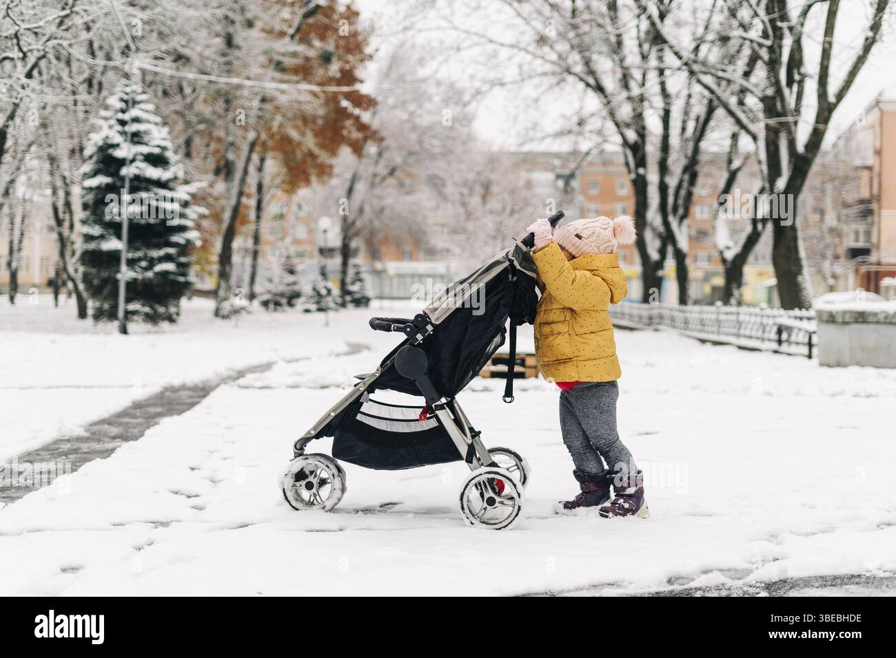 Kleinkind schiebt Kinderwagen mit Geschwistern darin. Wintertag mit Schnee. Weihnachten. Stockfoto