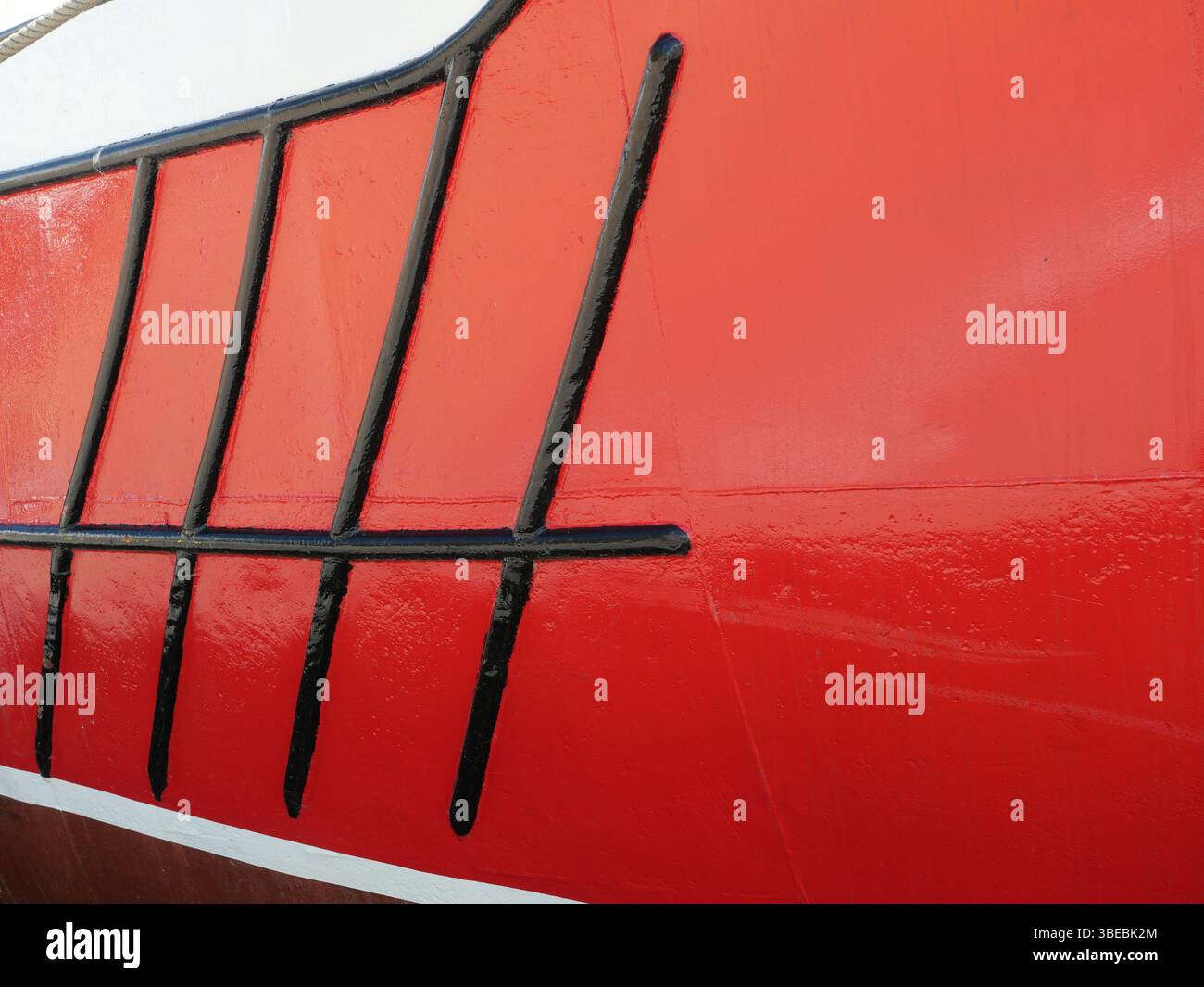 Roter Rumpf eines Fischerbootes mit schwarzen Streifen. Starker visueller Kontrast. Kopierraum. Platz für Texte und Designs. Stockfoto