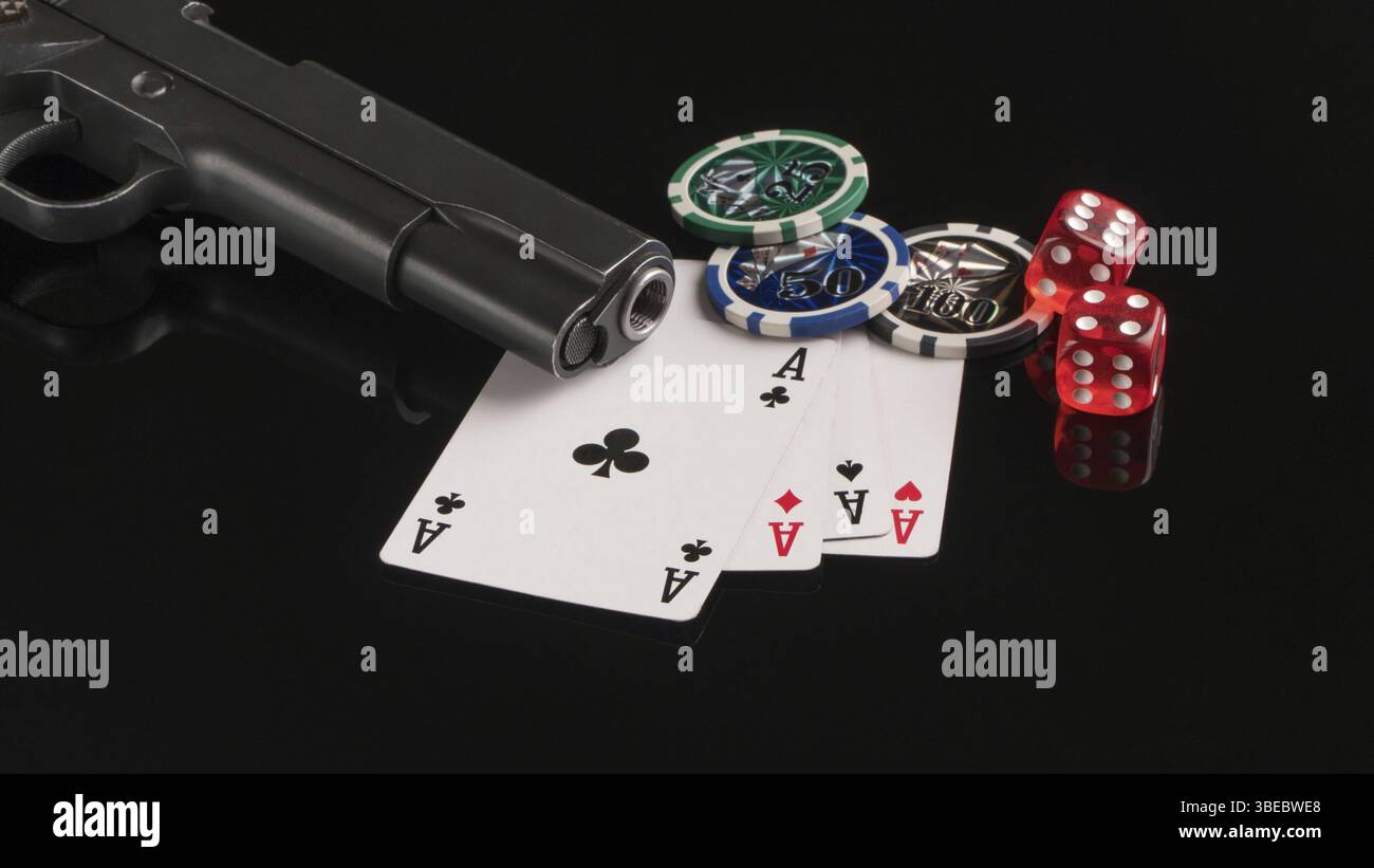 Ein Winkelschuss einer Waffe neben einigen Spielkarten und Würfeln auf einer schwarzen reflektierenden Oberfläche Stockfoto