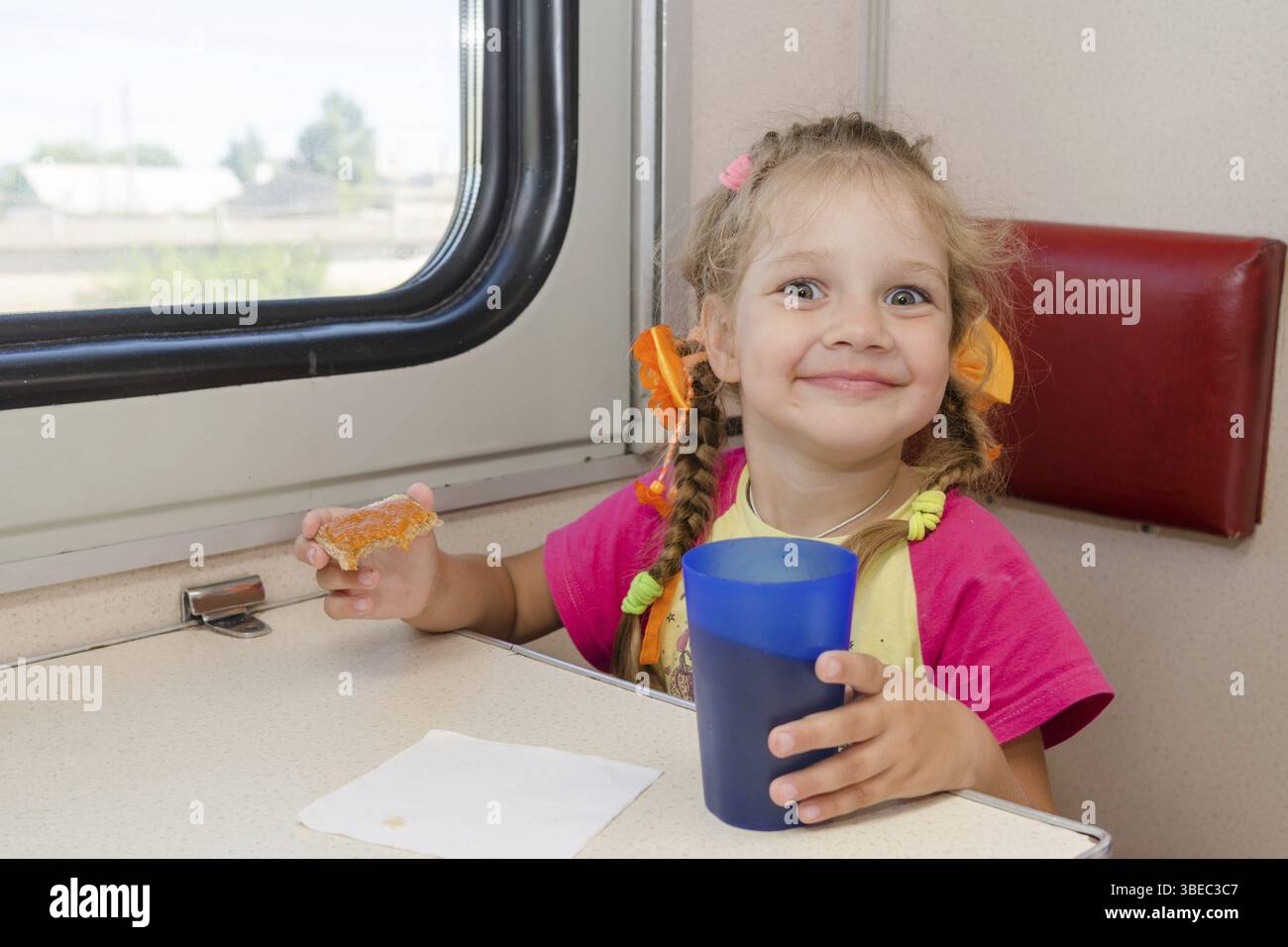 Kleines Mädchen mit einem Smiley trinken Tee mit einem Sandwich mit dem Zug an den Tisch bei Außenbordmotoren zweiter Klasse Wagen Stockfoto