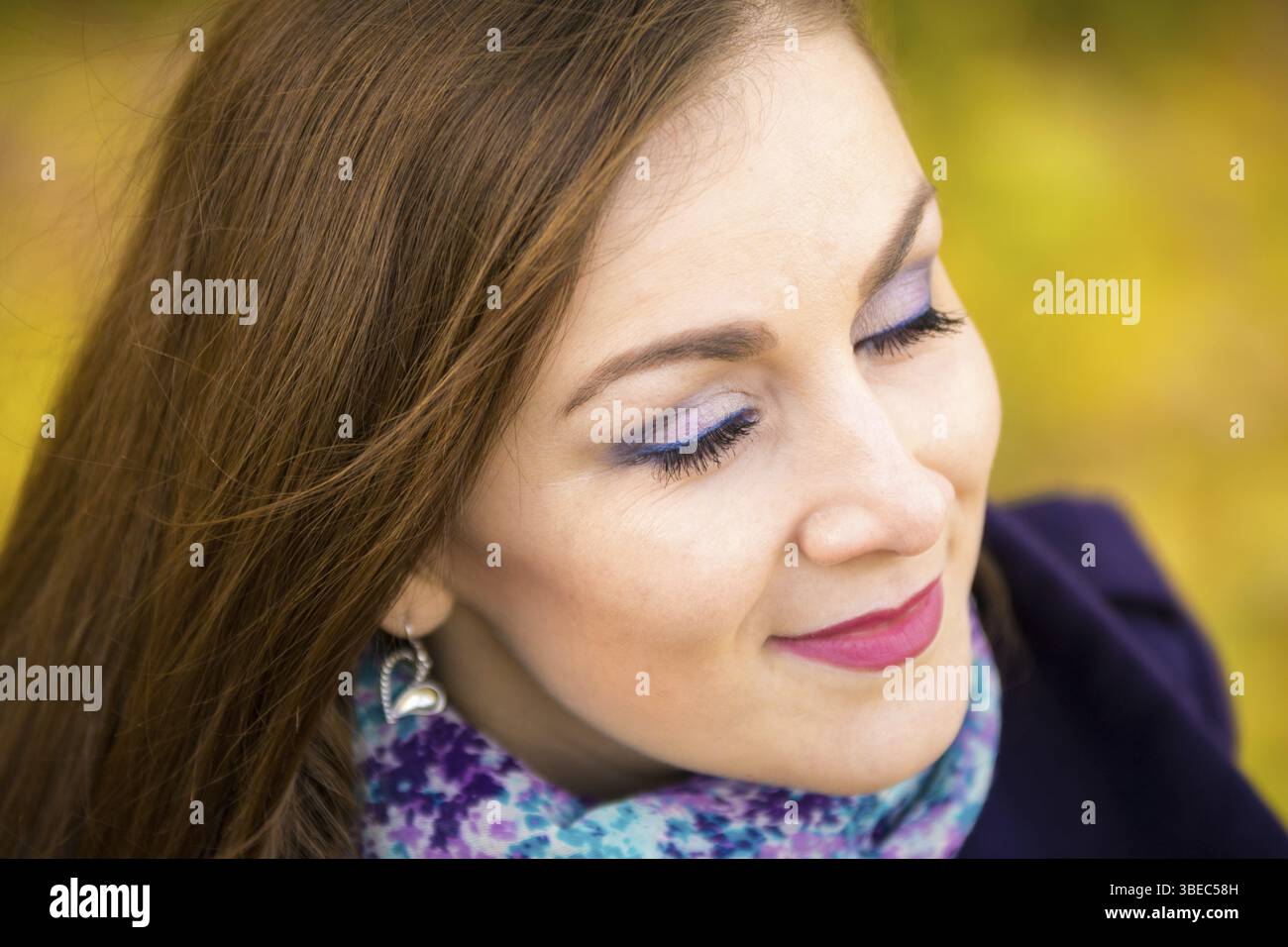 Reiben Sie ein schönes Mädchen mit geschlossenen Augen auf einem unscharfen Hintergrund von Herbstlaub Stockfoto