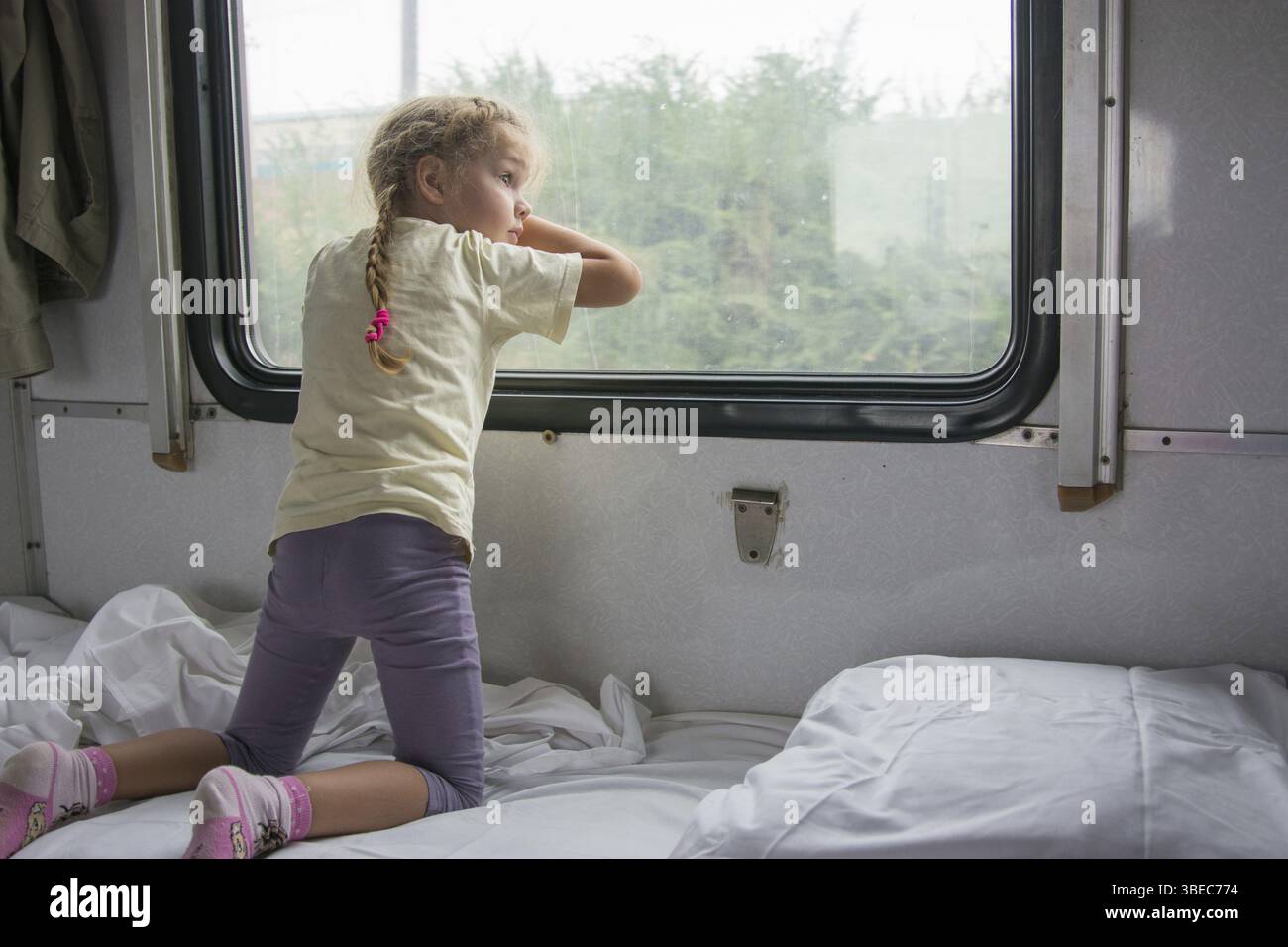 Vierjährige Mädchen schaut aus dem Fenster mit der Unterseite des Regals im Wagen zweiter Klasse Zug Stockfoto