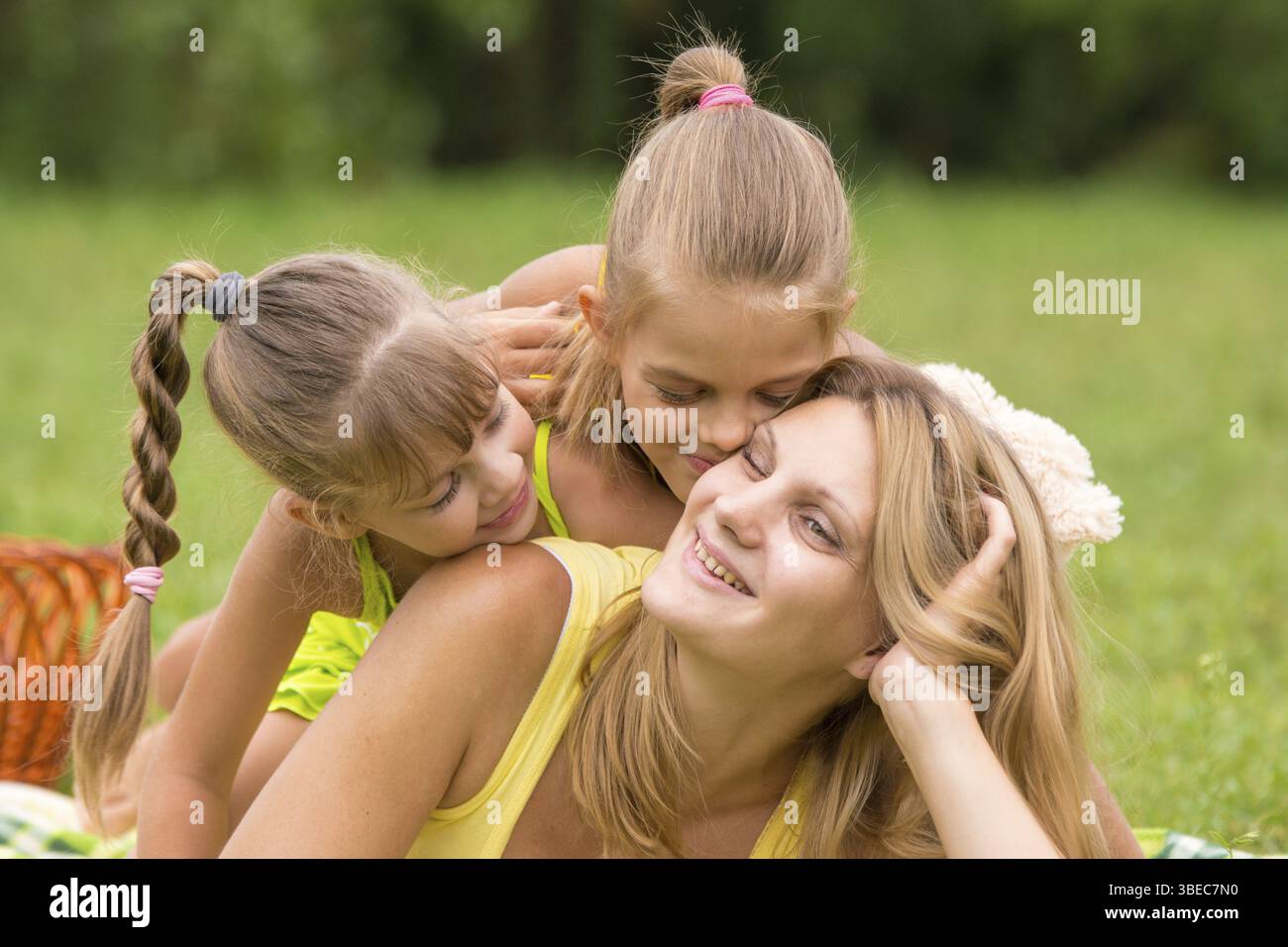 Zwei Töchter küssen und umarmen ihre Mutter liegen auf der Wiese ein Picknick Stockfoto
