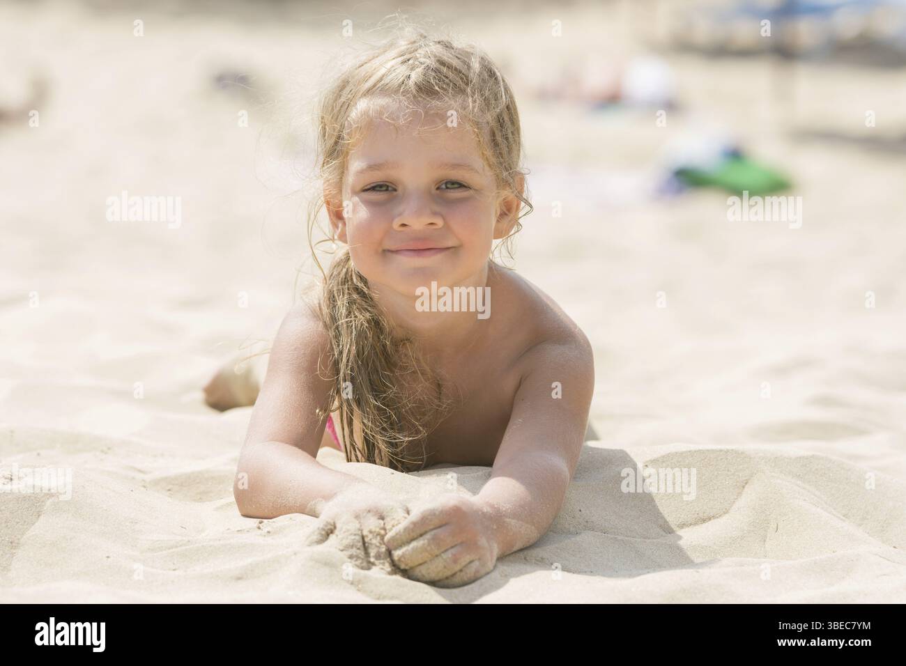 Hübsche Mädchen vier Jahre liegen im Sand auf dem Bauch am Strand an einem sonnigen Tag Stockfoto