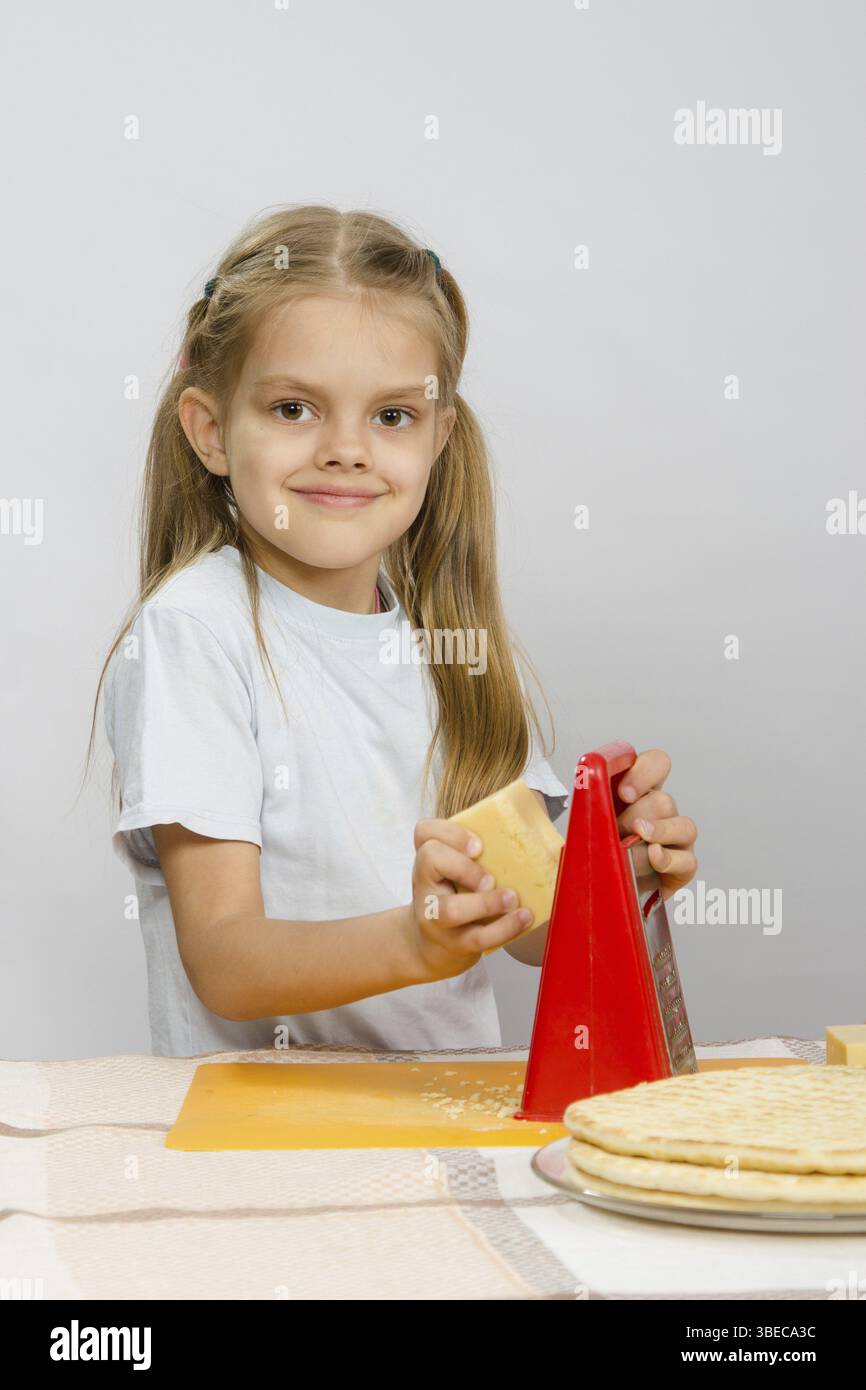 Sechsjährigen Mädchen posiert auf dem Küchentisch mit Käse und ein Reibeisen in den Händen der Stockfoto