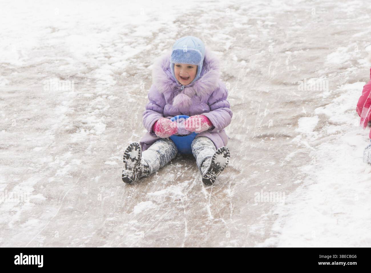 Fünfjährigen Mädchen reiten Winter auf einem schneebedeckten Hügel, umgeben von anderen Kindern Stockfoto