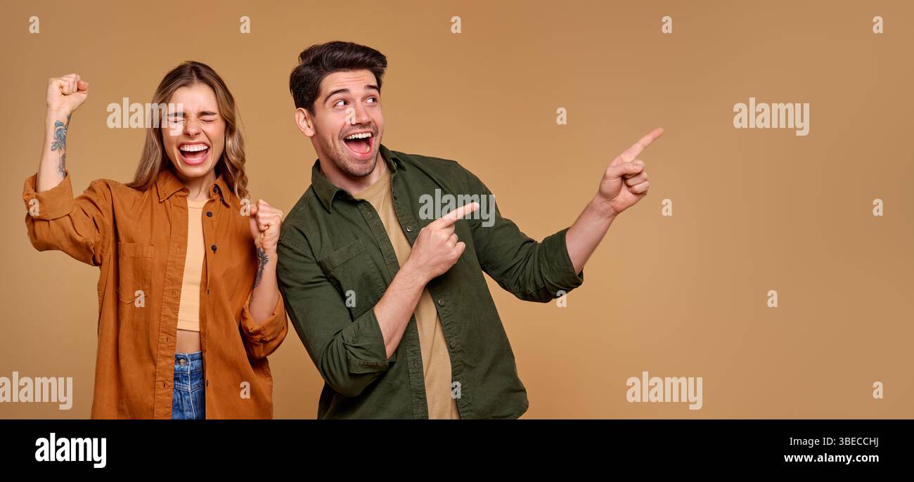 Ein fröhliches Paar drückt seine Begeisterung durch lebhafte Gesten aus, zeigt und lächelt sich gegenseitig an. Dieses Image eignet sich hervorragend für Werbeaktionen, Marketing und e Stockfoto
