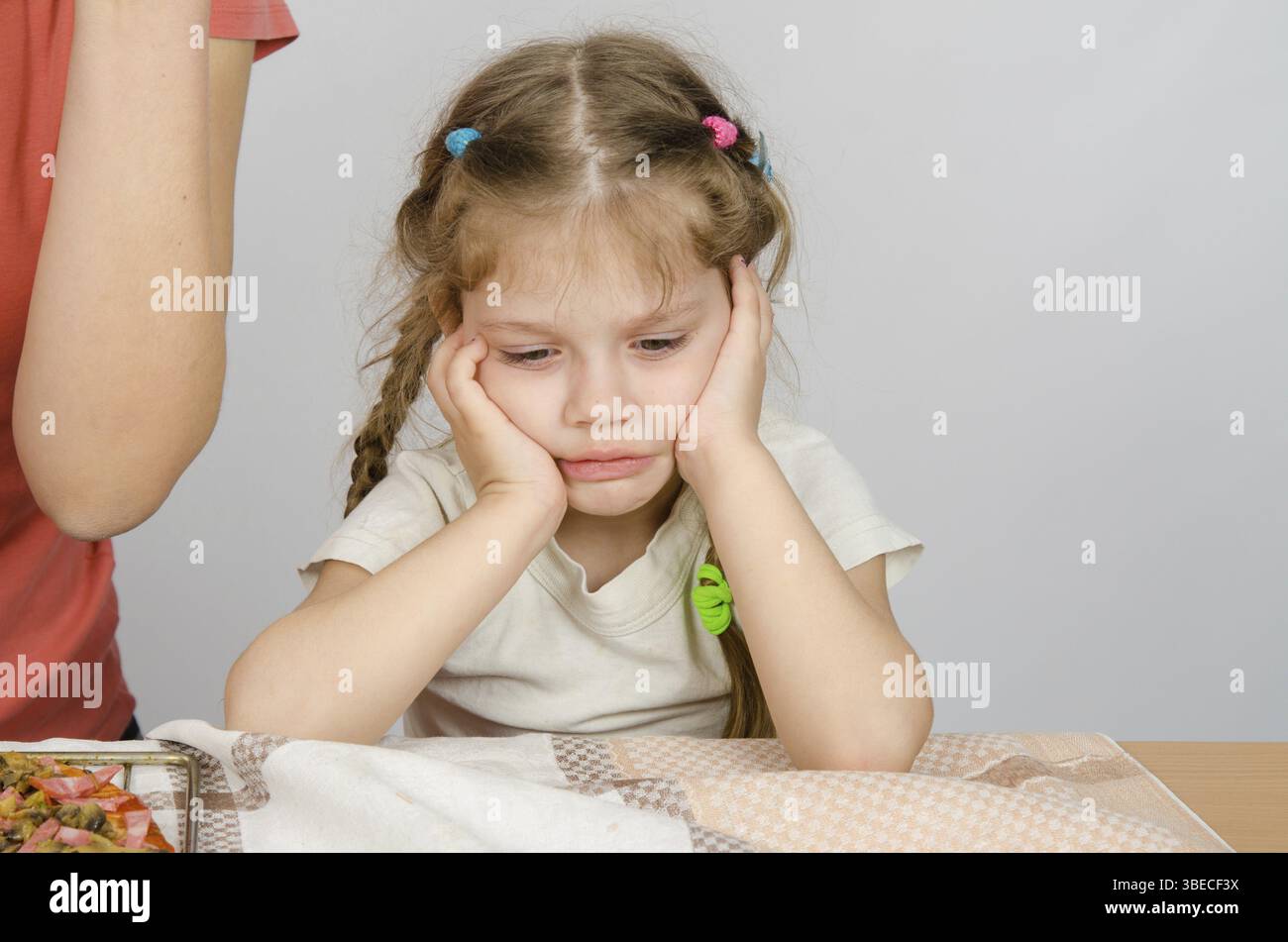 Das Babymädchen mit einem traurigen Ausdruck auf ihrem Gesicht sitzen am Küchentisch Stockfoto