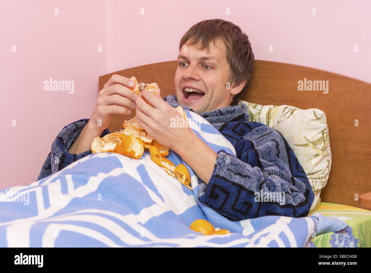 Mann im Bett liegend und Mandarinen Essen Stockfoto